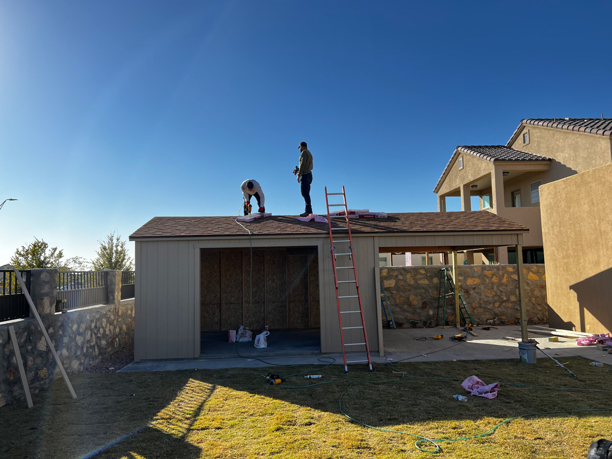 A large beige shed being built with two builders on the roof in El Paso.