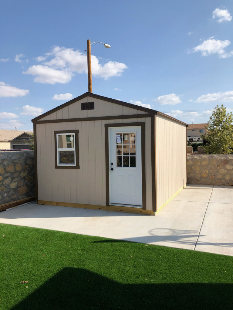 A beige shed with a white door in the backyard of an El Paso home.