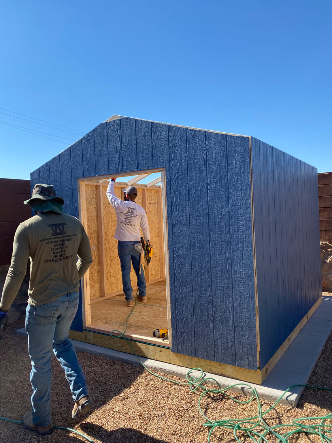Two people building a blue shed in El Paso.